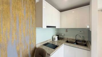 A compact kitchen with white cabinets, a granite countertop, a sink, and a kettle.