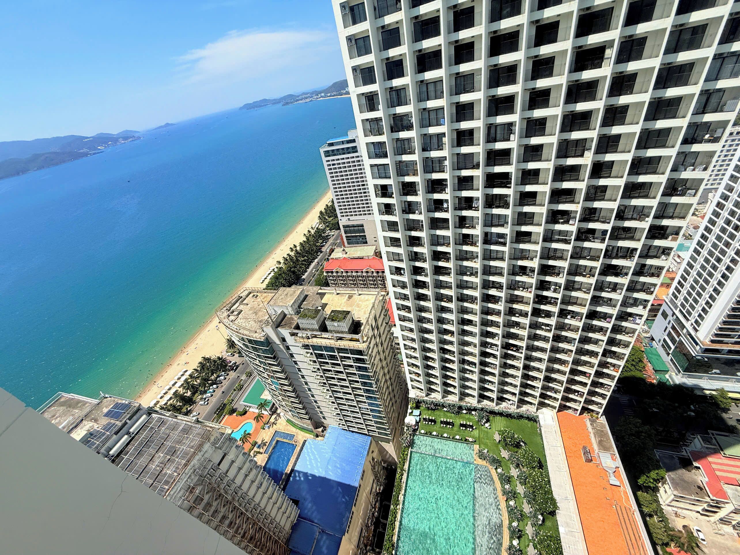 A high-rise building with a rooftop pool and a beach view.