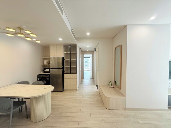 A modern kitchen with a built-in refrigerator, a dining area with a round table and chairs, and a hallway leading to an open space. - Apartment Lotte 2 (Nha Trang)
