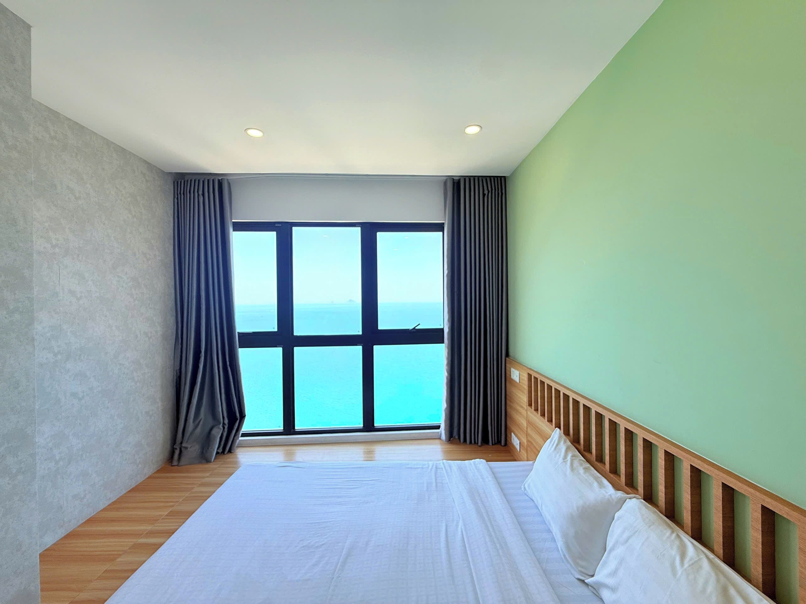 A bedroom with a large bed, a view of the sea, and a green wall.