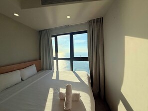 Habitación de hotel con una cama grande, cabecero y vista al mar a través de una ventana.