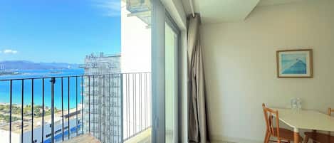 A balcony with a view of the sea and buildings, a dining table with chairs, and a painting on the wall.