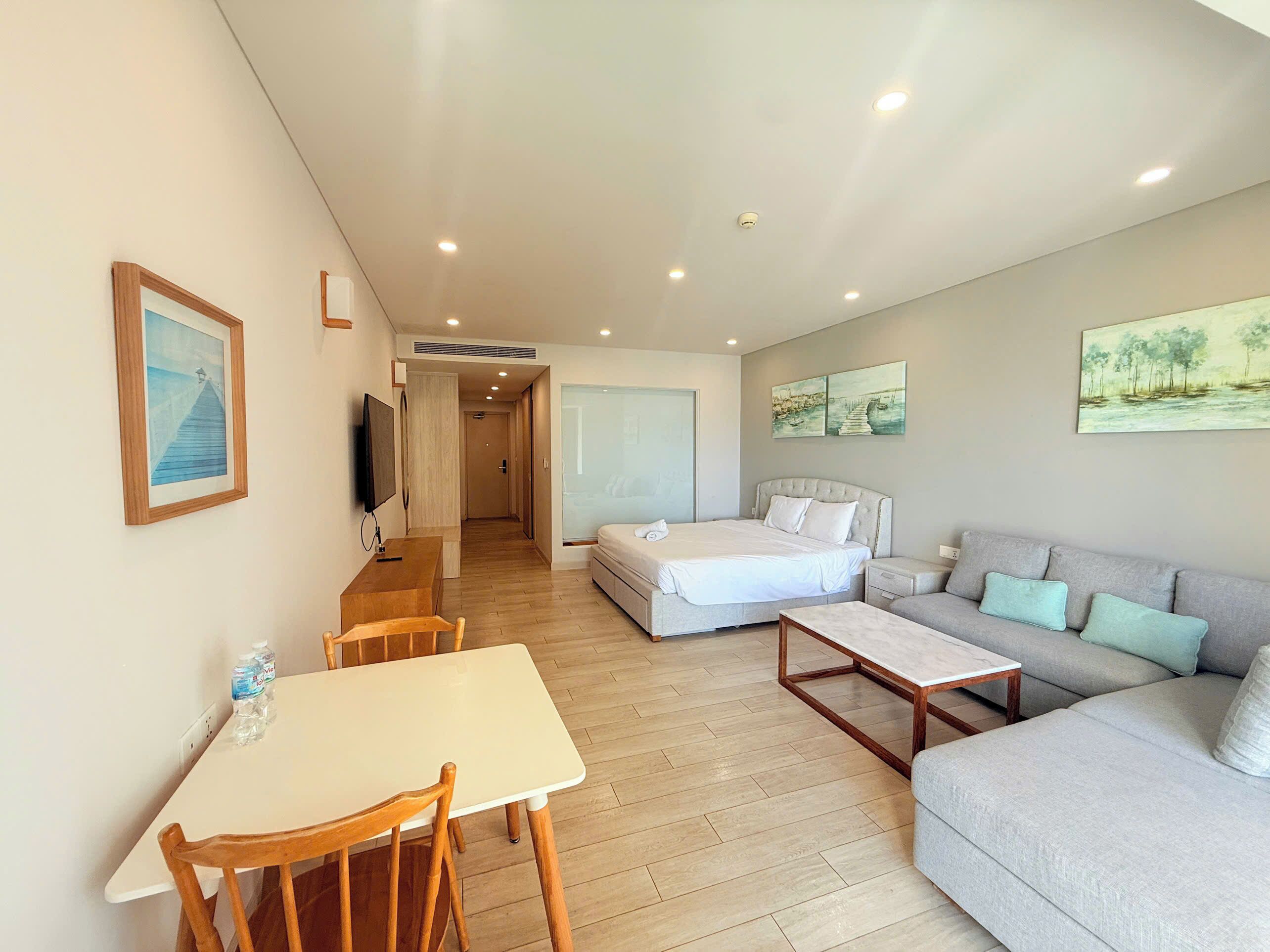 A hotel room with a bed, a sofa, a dining table with chairs, and artwork on the walls.