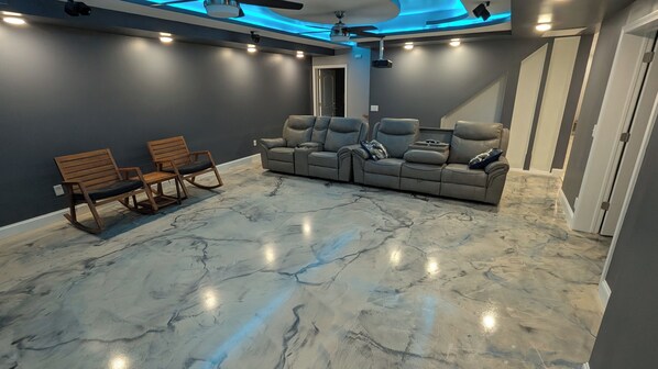 Una sala de cine en casa con piso de mármol, un sofá modular y dos mecedoras.