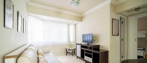 A living room with a sofa, a television on a stand, a ceiling fan, and a window with curtains.