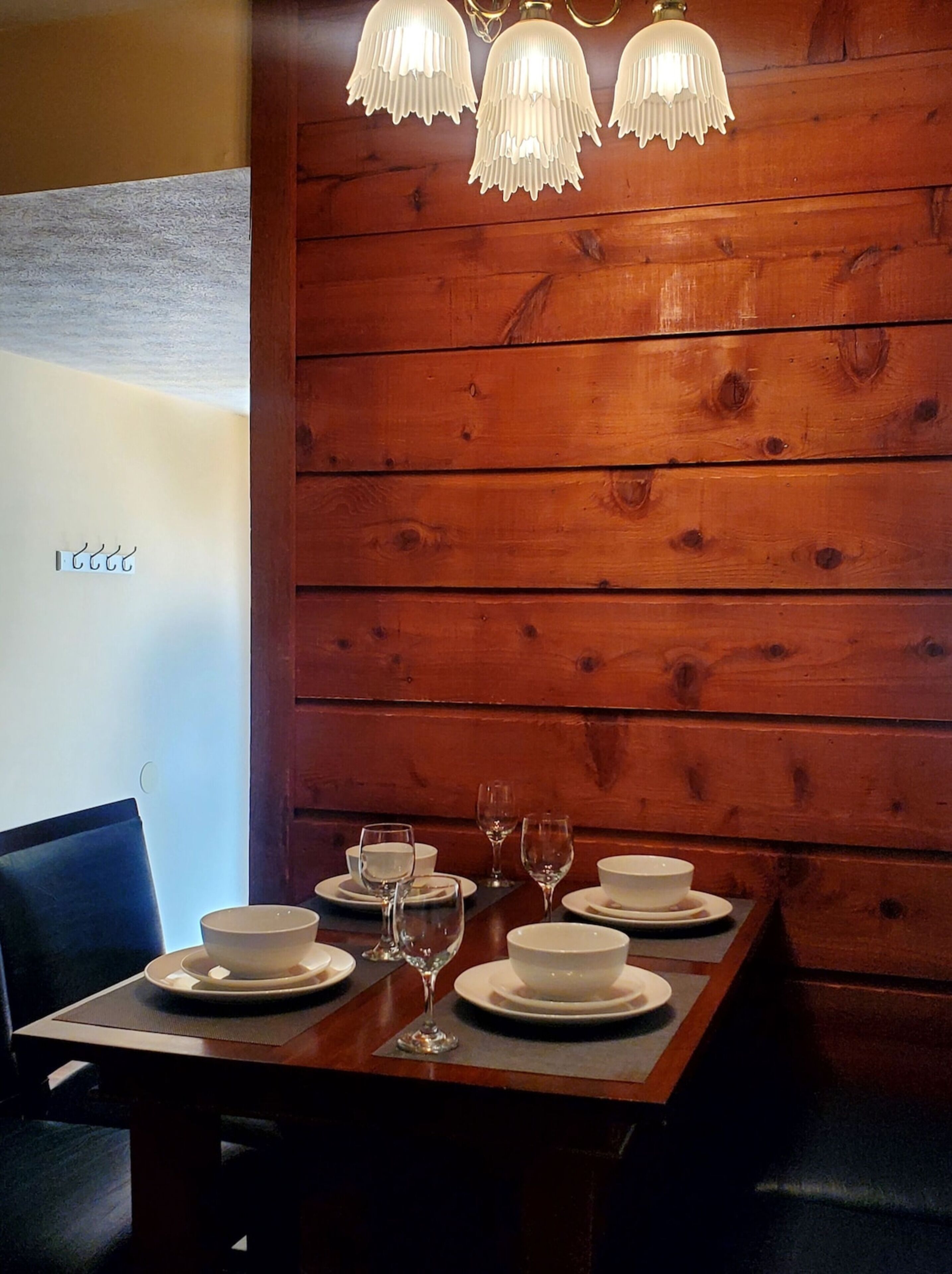 Pared revestida de madera con una mesa dispuesta para comer, que incluye platos, tazones y copas de vino.