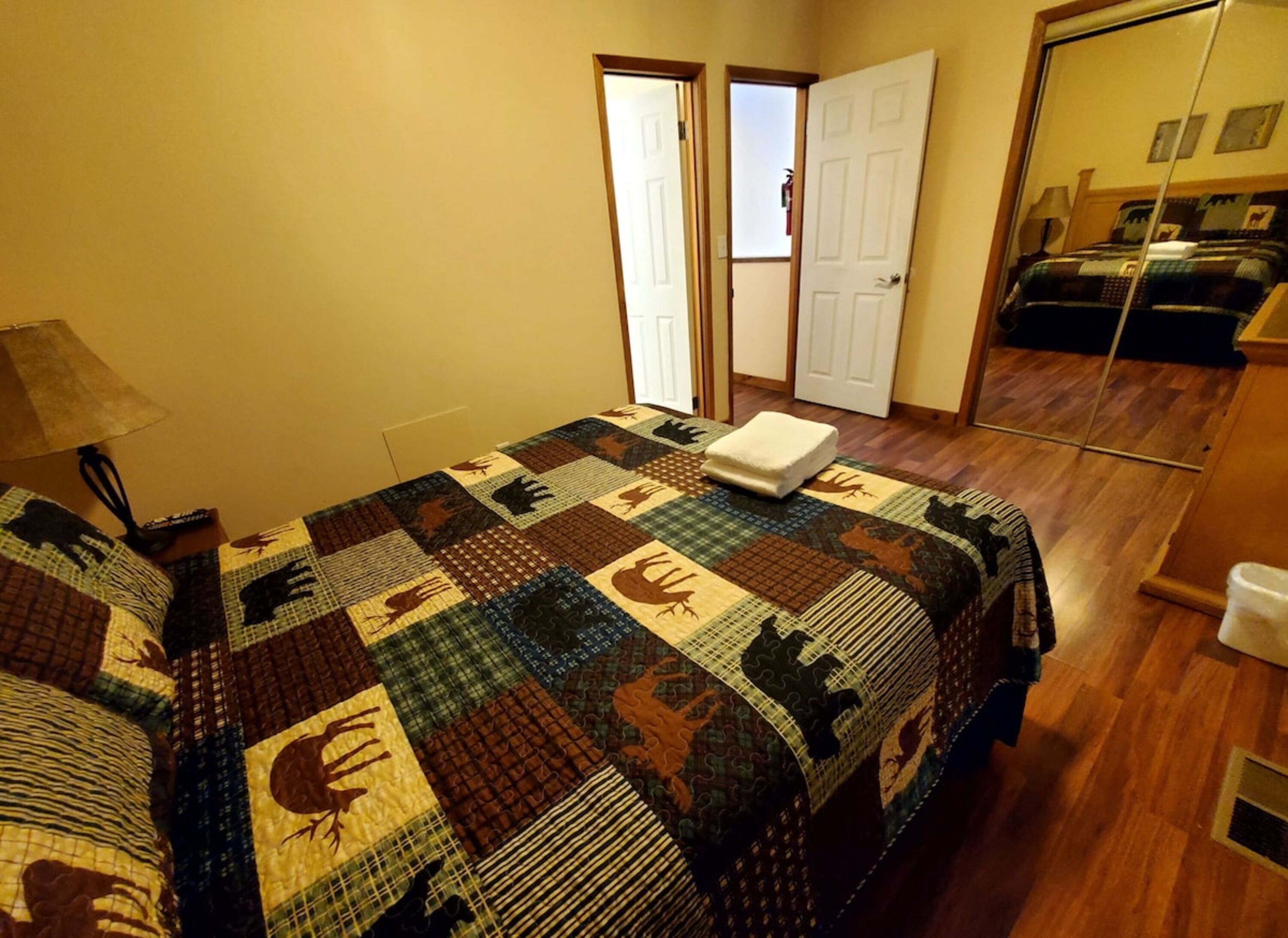 Een slaapkamer met een gewatteerde spreideken, een bedlampje en een deur naar een andere kamer.