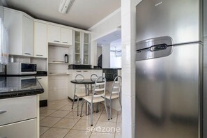 Une cuisine moderne avec des meubles blancs, un réfrigérateur en acier inoxydable, un four à micro-ondes et un coin repas comprenant une table ronde et des chaises.