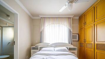 Quarto com cama, guarda-roupa, chuveiro e janela com cortinas.