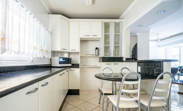 A modern kitchen with white cabinetry, a black countertop, and a dining area with a round table and chairs.