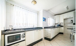 Une cuisine avec des meubles blancs, une cuisinière, un four à micro-ondes et un coin repas comprenant une table et des chaises.