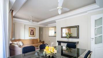 A modern living room with a glass dining table, a sofa, and a ceiling fan.