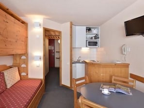 A compact room with a bed, a small table with a book, a microwave, and a TV mounted on the wall.