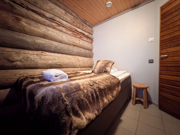 A log cabin-style bedroom with a bed, a small wooden stool, and a white door. - Sielikkö Aurora Log Villas (Saariselkä)
