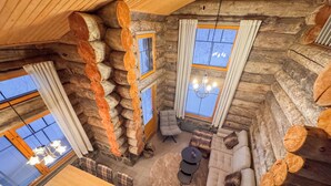Ein Holzblockhaus-Interieur mit Essbereich, Sofa und zwei mit Vorhängen versehenen Fenstern.