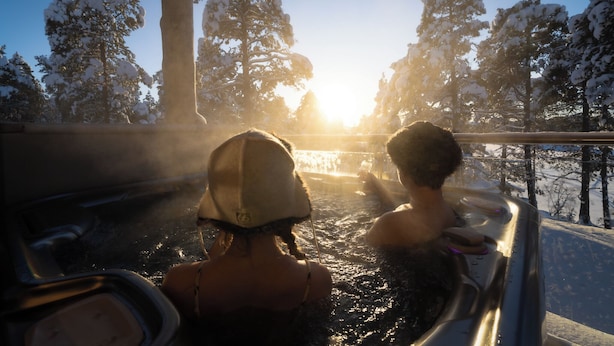 Zwei Personen in einer Badewanne mit verschneiter Landschaft und Bäumen im Hintergrund.