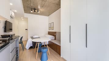 Quarto moderno e compacto com cozinha compacta, cama com encosto, mesa de jantar redonda e poltrona azul.