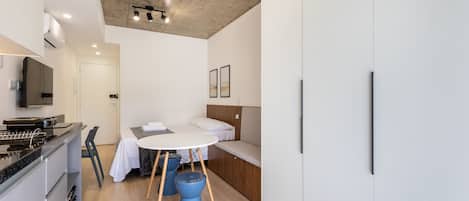 A compact, modern room with a kitchenette, a bed with a headboard, a round dining table, and a blue accent chair.