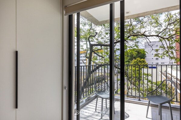A balcony with a metal railing, a chair, and a view of a tree and buildings. - Modern w/ Grill 5 min From PUC Ebi0303 (Curitiba)
