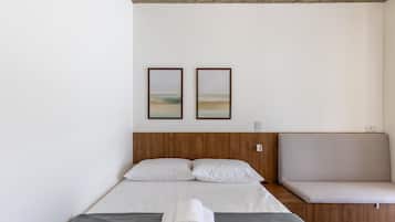 Quarto de hotel moderno com cabeceira de madeira, cama com roupa de cama branca, sofá cinzento e duas imagens emolduradas na parede.