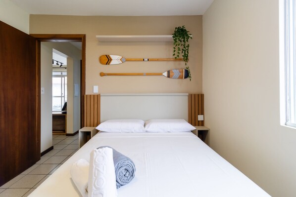 Habitació d'hotel amb un llit gran, dues taules de nit, un panell de capçalera de fusta i dos atuells decoratius a la paret.
