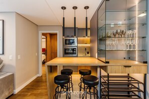 A modern kitchen with a central island, bar stools, a glass display cabinet, and built-in appliances.