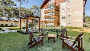 Een terras buiten met houten stoelen en een tafel, omgeven door een verzorgd gazon en een gebouw met meerdere balkons.