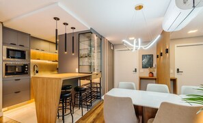 A modern kitchen with built-in appliances, a central island with bar stools, and a dining area with a white table and chairs.