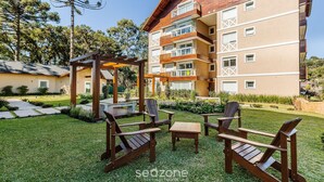 An outdoor seating area with wooden chairs and a table, surrounded by a well-maintained lawn and a building with multiple balconies. - Cozy Themed Apartment in Canela Dal221 (Canela)