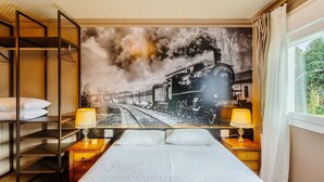 A hotel room with a large bed, two bedside tables with lamps, a bunk bed, and a large wall mural of a train. - Cozy Themed Apartment in Canela Dal221 (Canela)