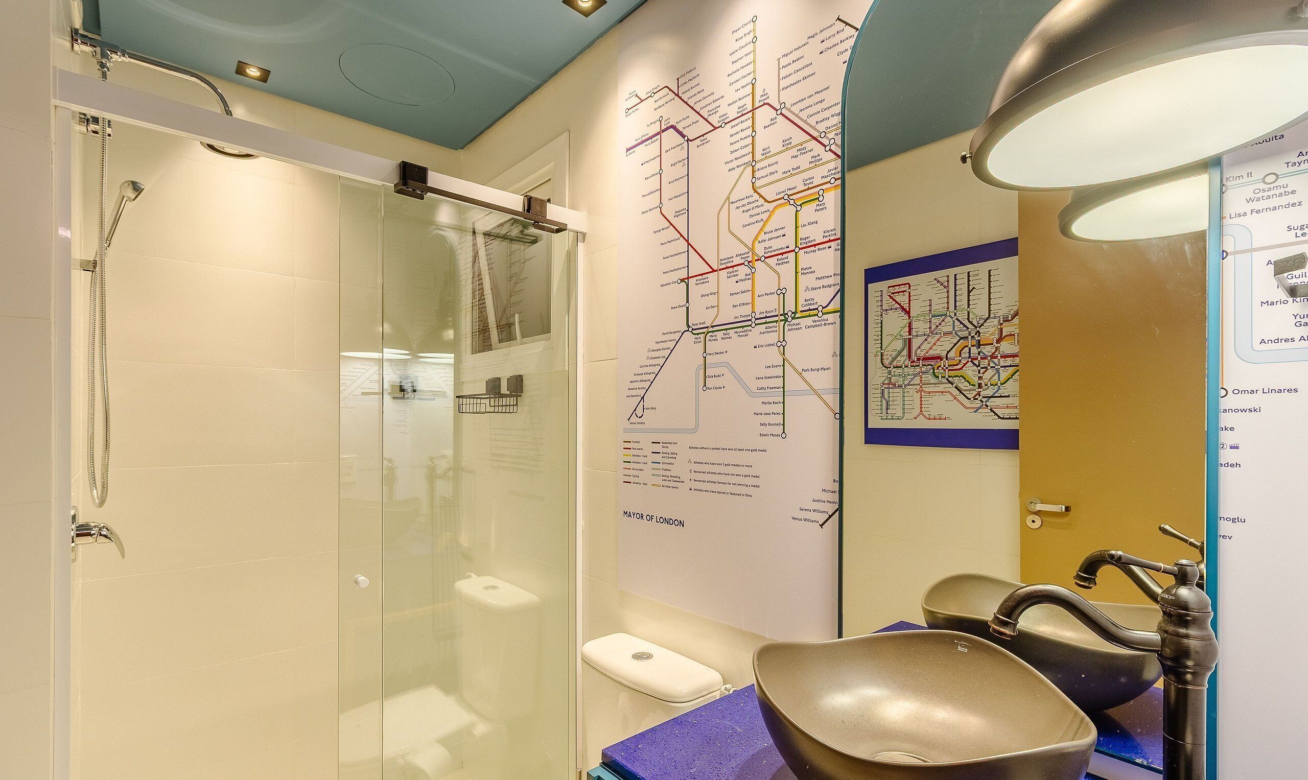 Un baño con cabina de ducha de vidrio, lavamanos con grifo moderno y un mapa del metro de Londres en la pared.