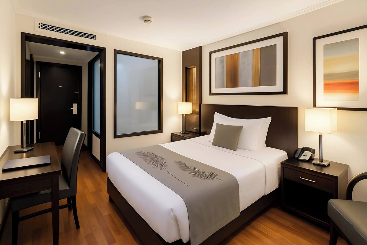 Una camera d'albergo con un letto grande, una scrivania, una sedia, un comodino e una televisione a parete.