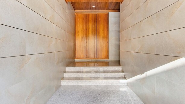 Una escalera moderna con una puerta de madera al final, que da a un cuarto con piso de baldosas y paredes revestidas.