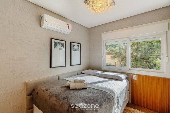 Un dormitorio con cama, equipo de aire acondicionado, cuadros enmarcados y ventana con vistas.