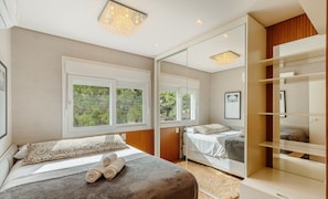 A bedroom with two beds, large windows, a mirror, and a built-in wardrobe.