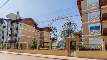 Un edificio residencial de varios pisos con balcones, una entrada protegida por un portón y una noria al fondo.