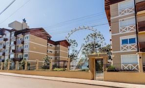 A multi-story residential building with balconies, a gated entrance, and a Ferris wheel in the background.