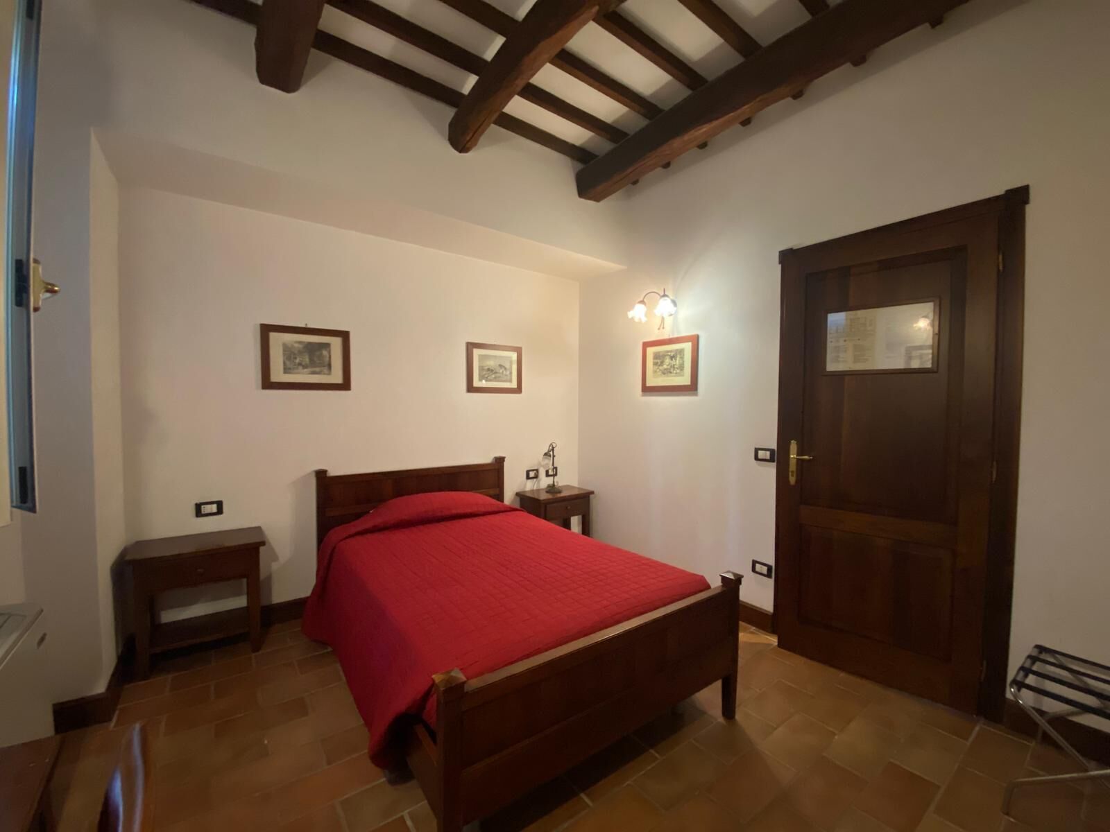 Une chambre à coucher avec un lit en bois, une table de chevet, une commode, une couverture rouge et une porte sur laquelle est affichée une note.