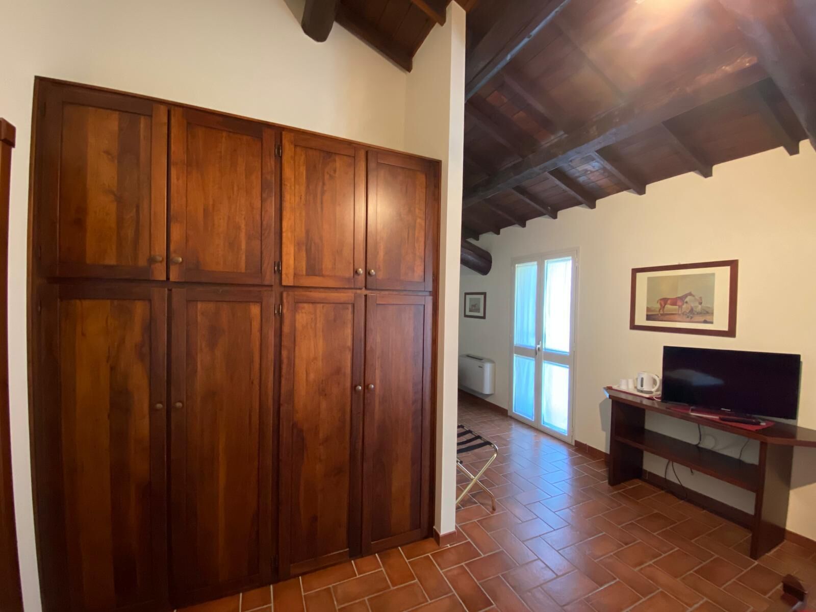 Ein Zimmer mit großem Holzschrank, einem Fernseher auf Holzfuß und Fliesenboden.