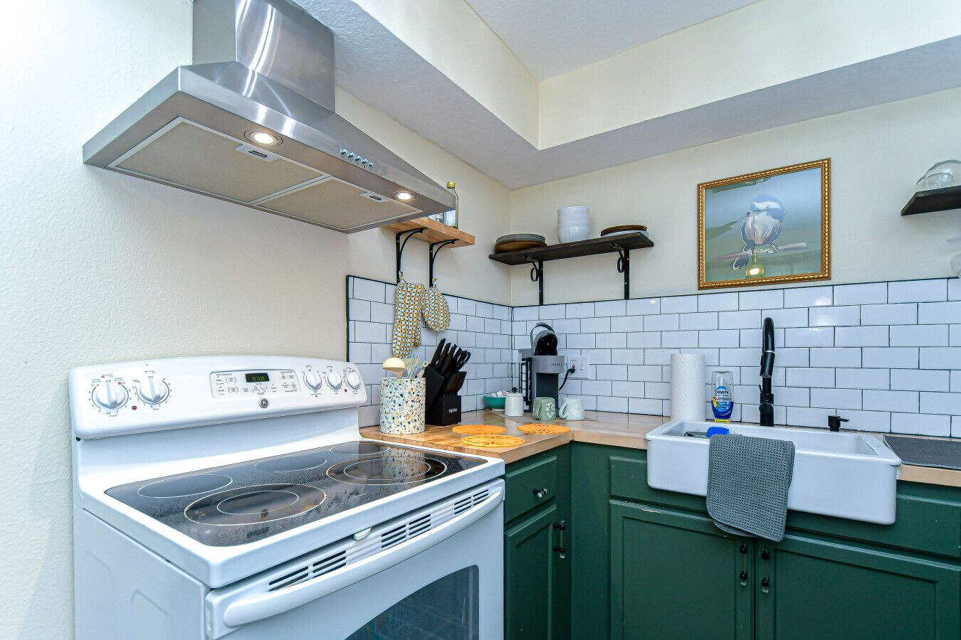 Een keuken met een wit fornuis, groene kasten, een roestvrijstalen afzuigkap en een betegelde spatwand.
