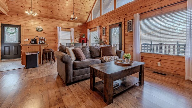 A cozy cabin interior with a wooden ceiling, a sofa, a coffee table, and a kitchen area. - Fall Vacation Available!-Indoor Jacuzzi-w/Outdoor Hot Tub & Arcade Game (Pigeon Forge)