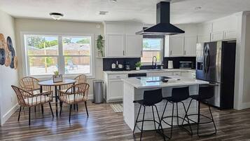 A modern kitchen with white cabinetry, a central island with bar stools, and a black range hood.