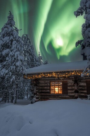 En træhytte med et oplyst vindue, omgivet af sneklædte træer og udsigt til nordlys.
