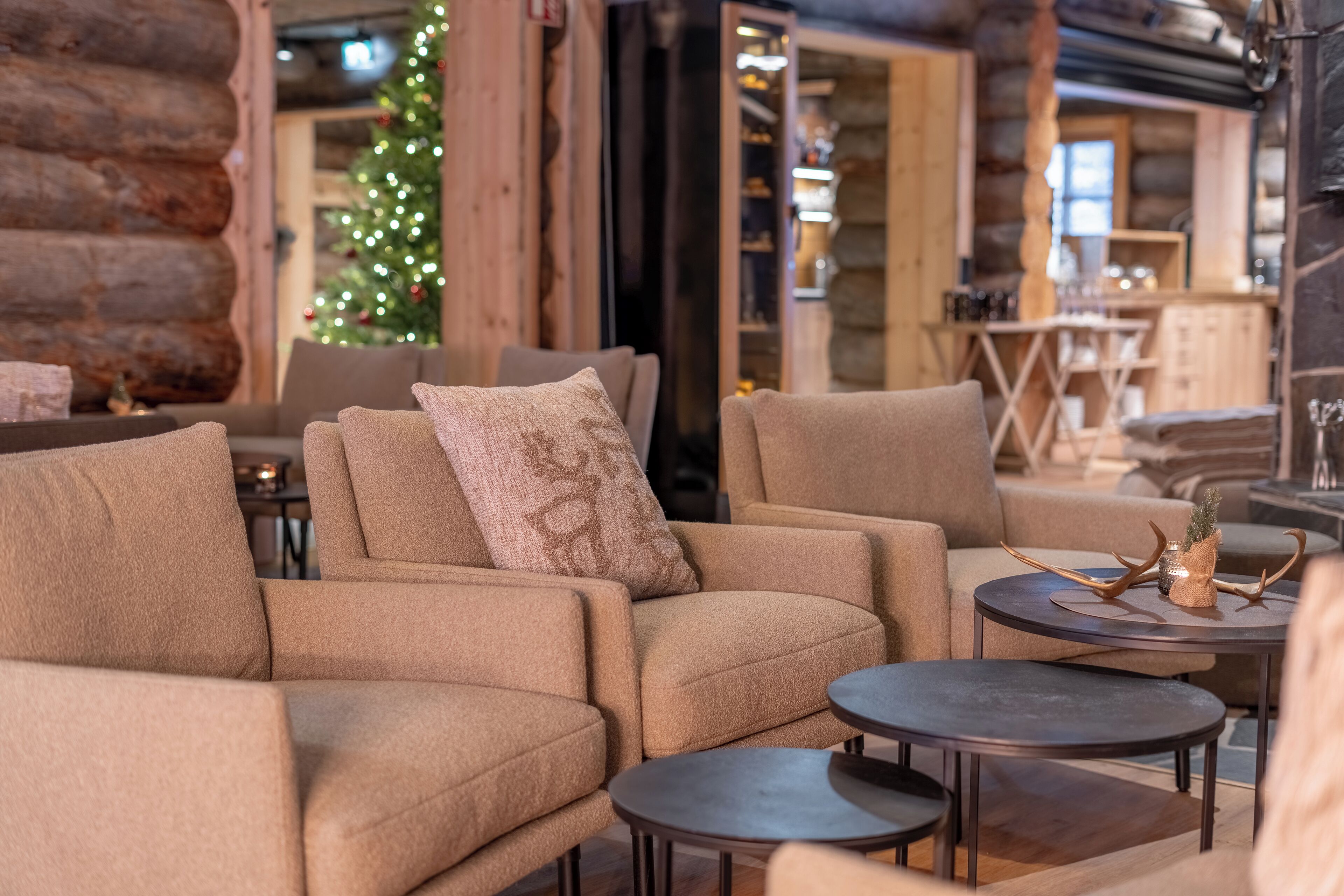 A cozy log cabin interior with a fireplace, plush beige sofas, and a Christmas tree.