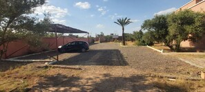 Ein gepflegter Schotterweg führt zu einem verschlossenen Eingang, unter einem Metallcarport steht ein Auto.