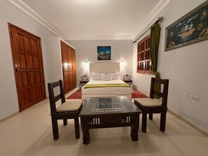 A hotel room with a bed, two bedside tables, a glass-top table with chairs, and a painting on the wall. - Villa-Riad 15 minutes from the center of Marrakech (Marrakech-Safi)