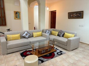 A living room with two grey sofas, yellow and silver cushions, a glass coffee table, and a patterned rug. - Villa-Riad 15 minutes from the center of Marrakech (Marrakech-Safi)