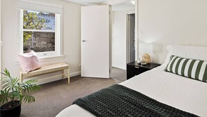 Een slaapkamer met een bed, een nachtkastje, een bankje bij het raam en een potplant.