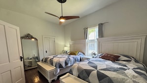 Un dormitorio con una cama tamaño reina, ventilador de techo, cómoda, espejo y ventana con cortinas.