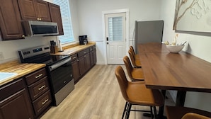Una cocina moderna con armarios de madera, microondas, estufa y un comedor con una mesa larga y sillas.
